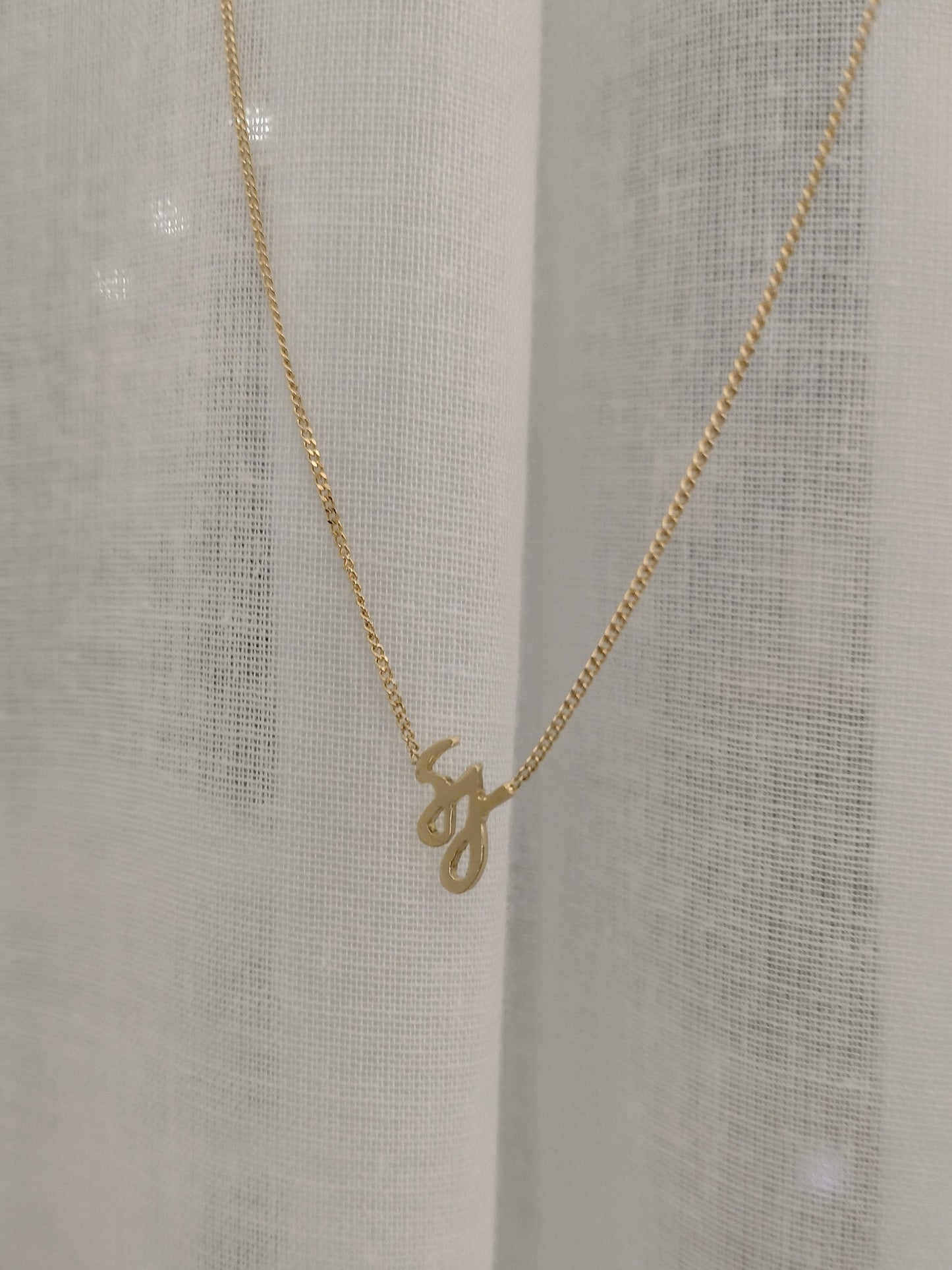 An 18 carat yellow gold pendant with initials S and J suspended from a delicate chain in 18 carat yellow gold. The necklace is available in custom order with different initials. Shown here on a white background.